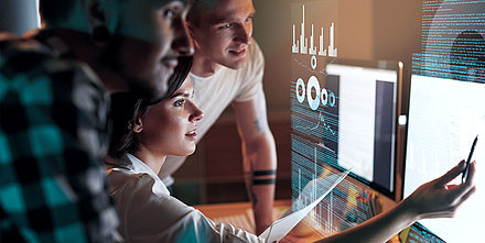 Entspanntes und übersichtliches Netzwerk-Monitoring mit der LANCOM Management Cloud Eine weibliche und zwei männliche IT-Mitarbeitende überwachen auf einem Dashboard ihr Netzwerk